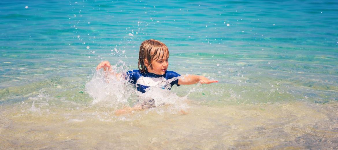 Bambino gioca felice nell'acqua cristallina di una spiaggia soleggiata.