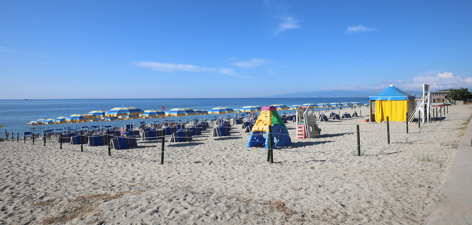 Spiaggia sabbiosa con ombrelloni colorati e area giochi per bambini, cielo limpido.