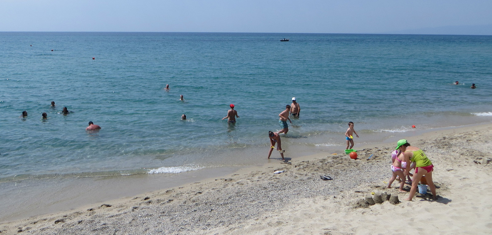 Spiaggia soleggiata con persone che nuotano e giocano sulla sabbia.