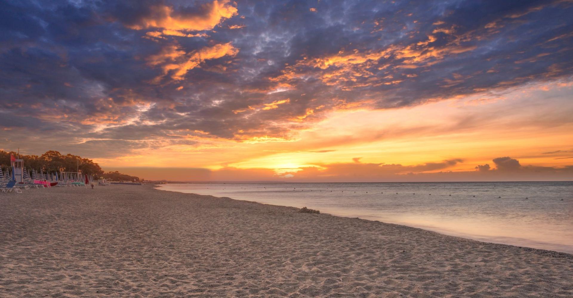 Spiaggia al tramonto con cielo nuvoloso e mare calmo.