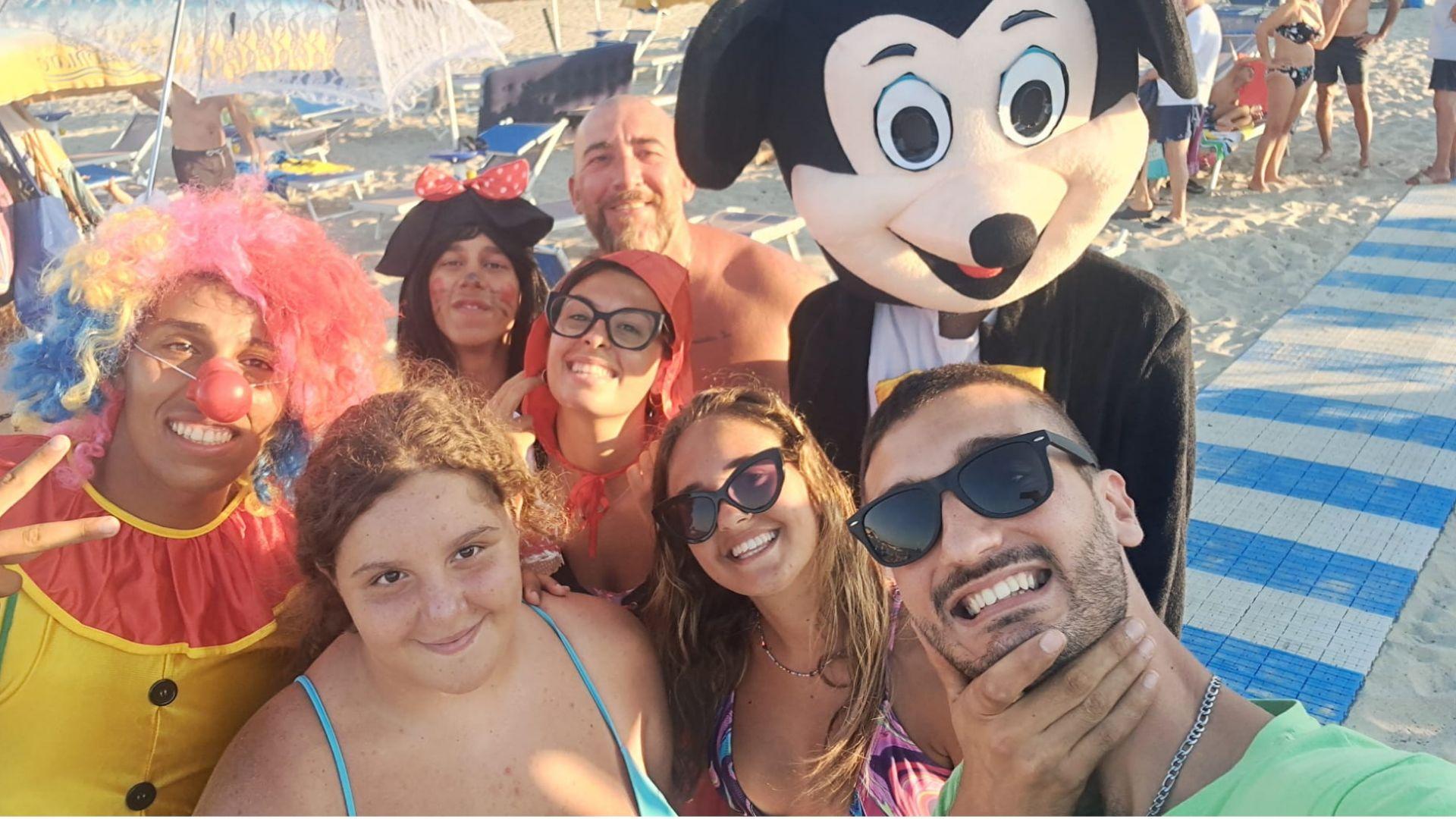 Gruppo in spiaggia con costumi colorati e maschere, sorrisi e atmosfera festosa.