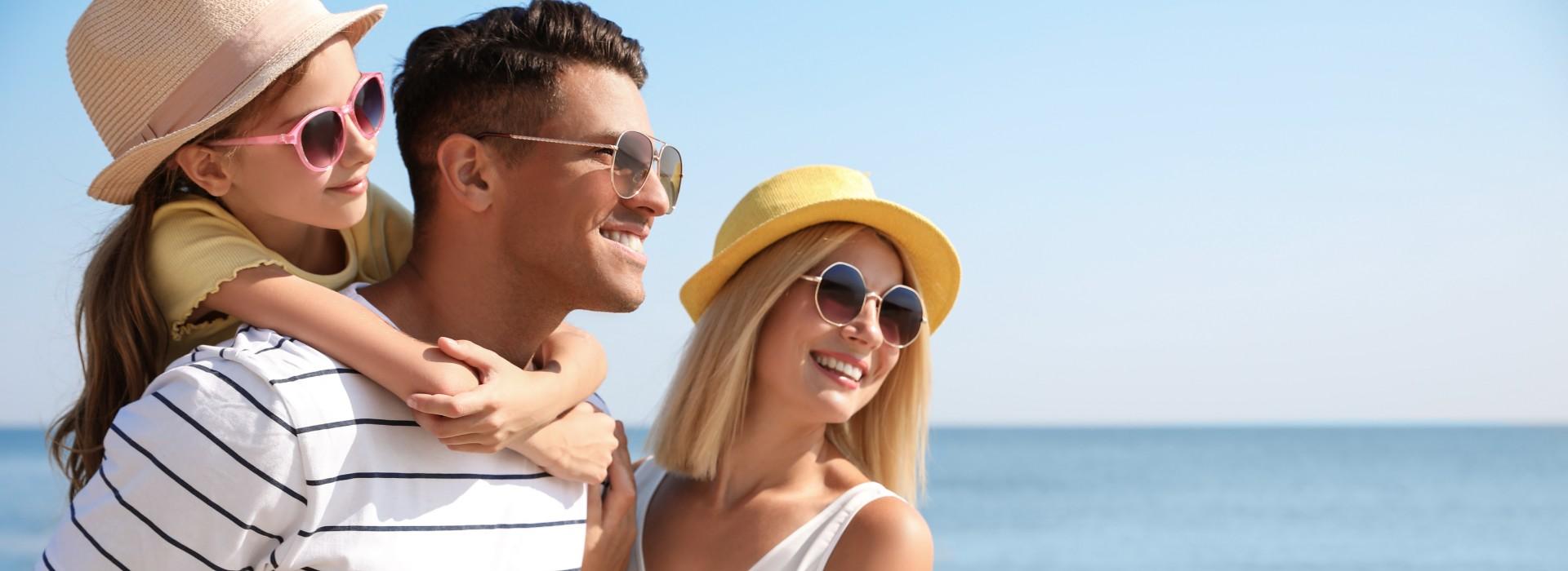 Famiglia felice in vacanza al mare, indossando occhiali da sole e cappelli.