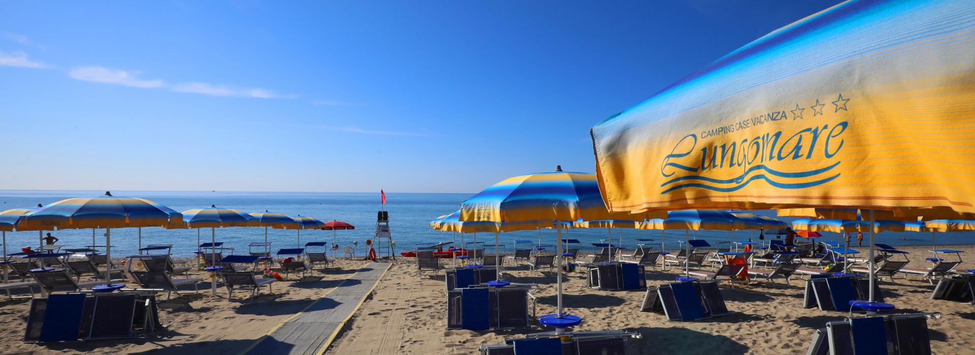 Spiaggia con ombrelloni gialli e blu, mare calmo e cielo sereno.