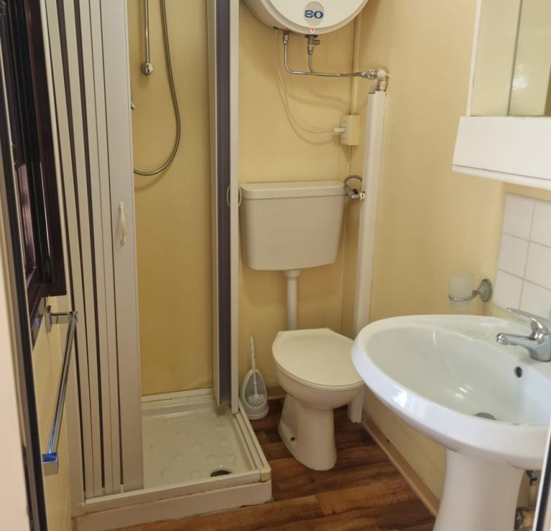 Bagno compatto con doccia, lavabo, WC e scaldabagno, pavimento in legno.