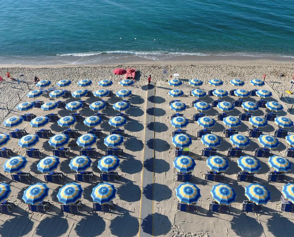 Spiaggia affollata con bagnanti e ombrelloni, mare cristallino e cielo sereno.